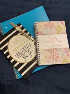 A stay at home mom’s tools. Blue notebook, Leave A Little Sparkle Wherever You Go Journal, silver watch, 2020 planner