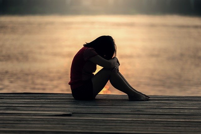 woman sitting alone on dock by water