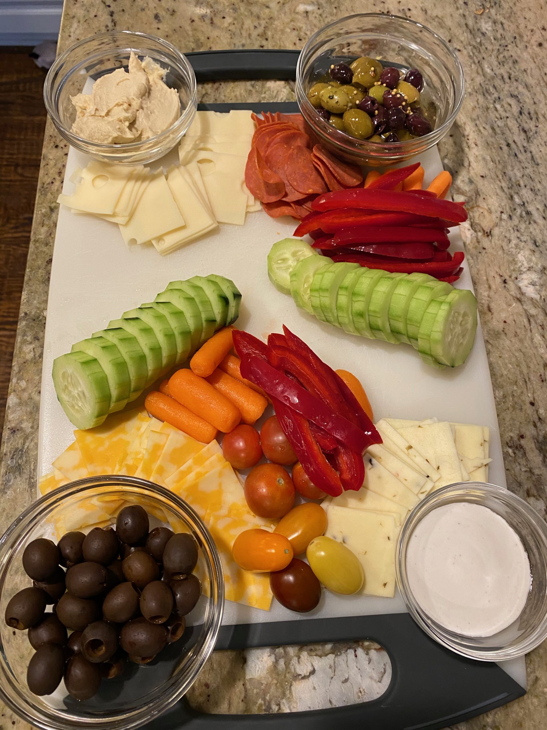 cutting board with dips, olives, cheese, meats, and veggies