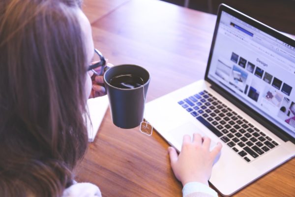 woman holding coffee and typing on computer