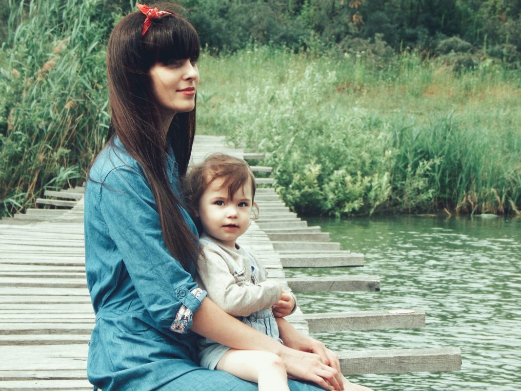 mother holding daughter on dock by water