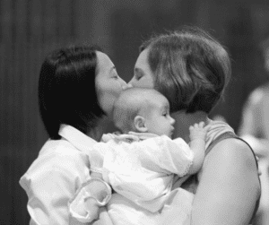 two women kissing while holding a baby