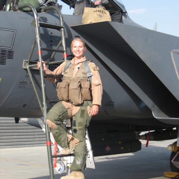 Woman in uniform standing on ladder in front of military jet