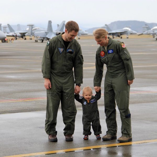 Man and Woman in military flight suits both holding the hands of a toddler