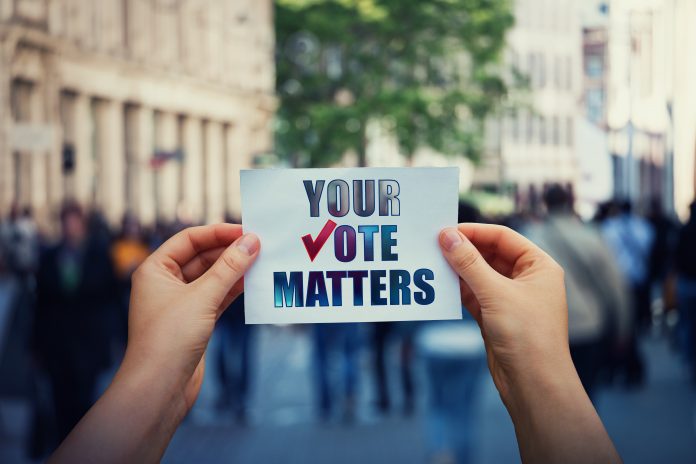 Hands hold a paper sheet with the message your vote matters over a crowded street background. People legal and democratic rights, every voice counts. Election campaign and electoral agitation concept your vote matters