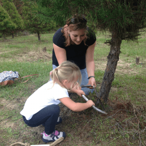 Woman helping little girl cut down a real Christmas Tree