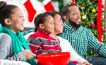 The Best Hallmark Christmas Movies for 2020 A family laughing while watching a movie together at the holidays