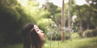 dark-haired woman blowing dandelion seeds in a field