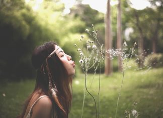 dark-haired woman blowing dandelion seeds in a field