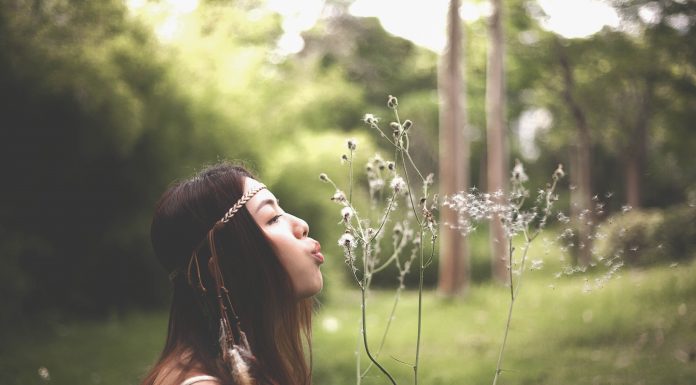 dark-haired woman blowing dandelion seeds in a field