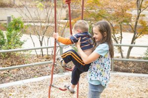 older sister helping younger brother on playground