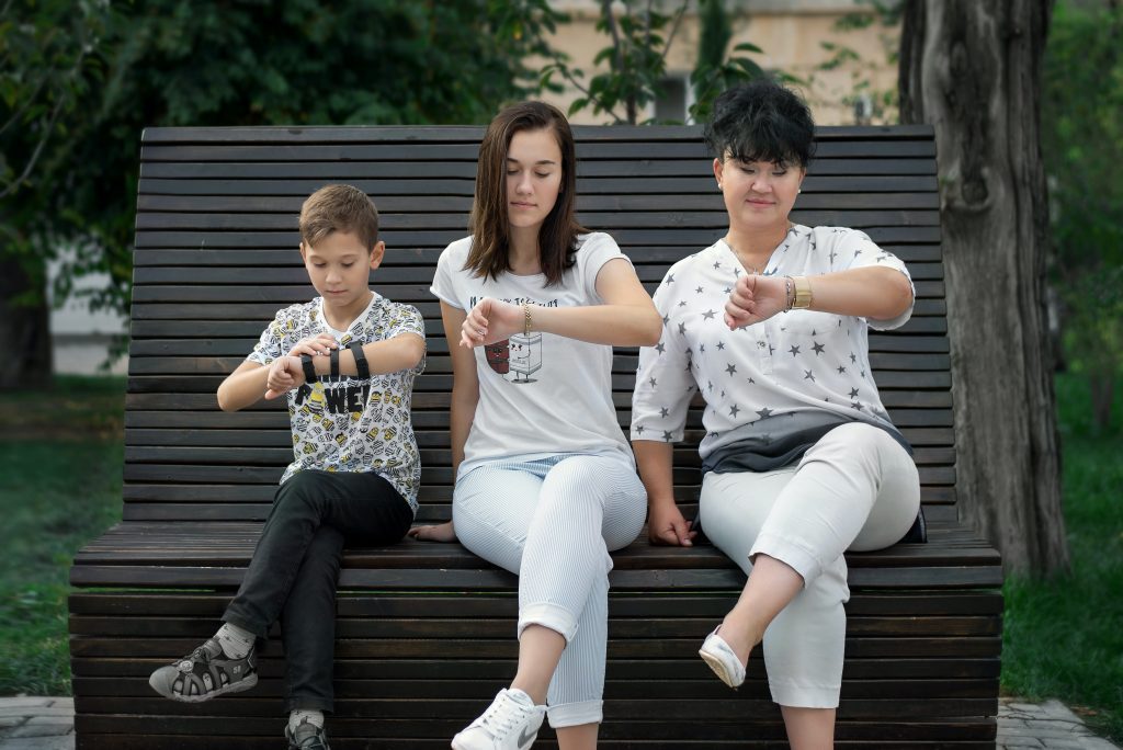 parents and child sitting on bench looking at watches