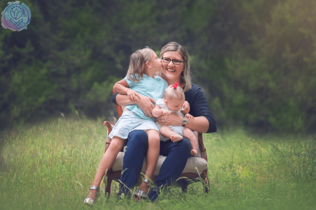 mother hugging 2 daughters on a chair in a field