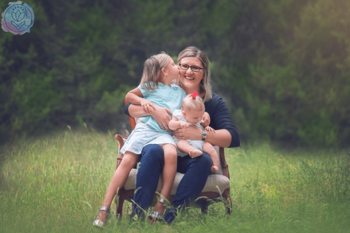 mother hugging 2 daughters on a chair in a field