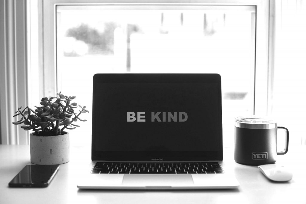 computer with be kind on screen on desk with plant and mug in black and white