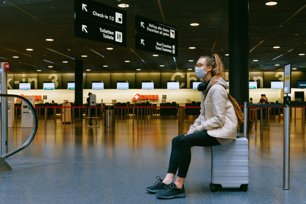 woman sitting on suitcase with mask on for travel during the pandemic