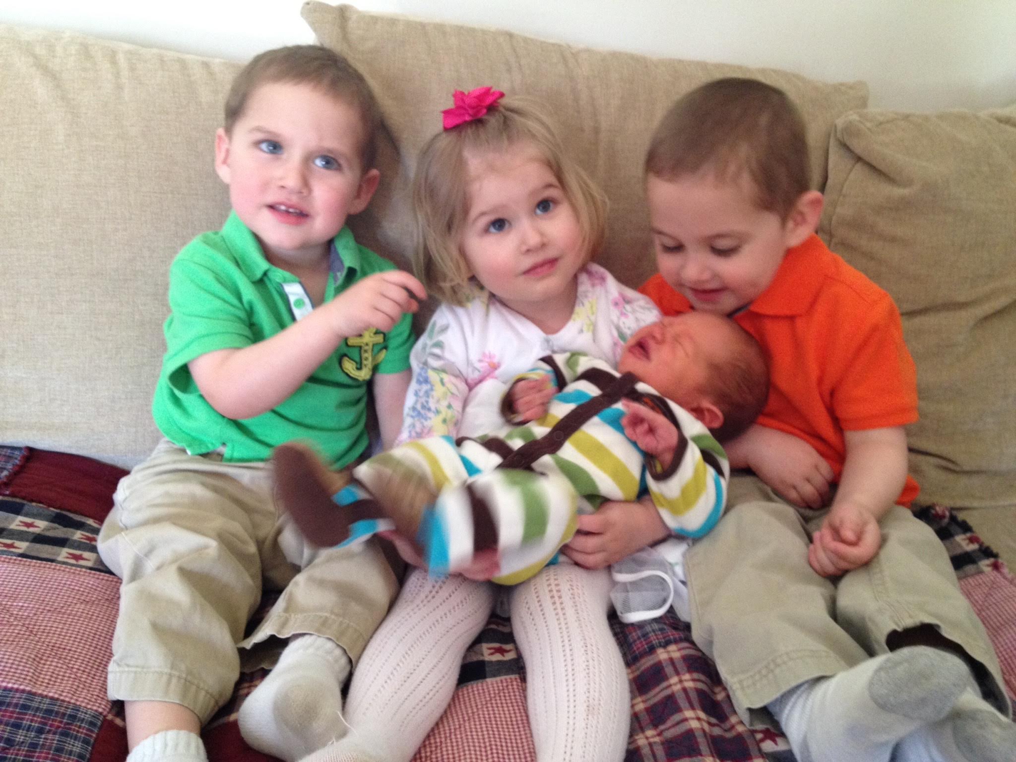 three children sitting on a couch holding a new baby