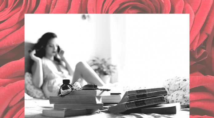 black and white photo of woman on bed in boudoir shoot with red rose background