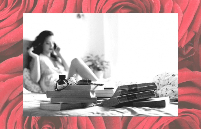 black and white photo of woman on bed in boudoir shoot with red rose background