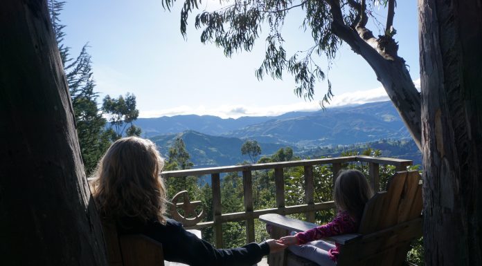 mom holding little girl's hand in porch chairs on a deck overlooking mountains