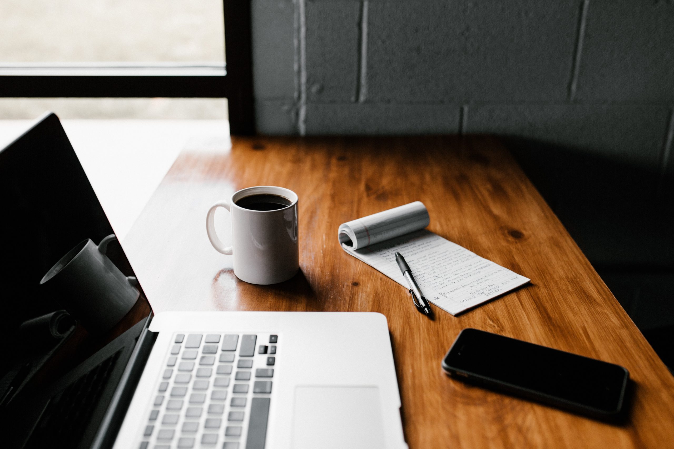 computer and coffee with notepad and phone on a wood desk