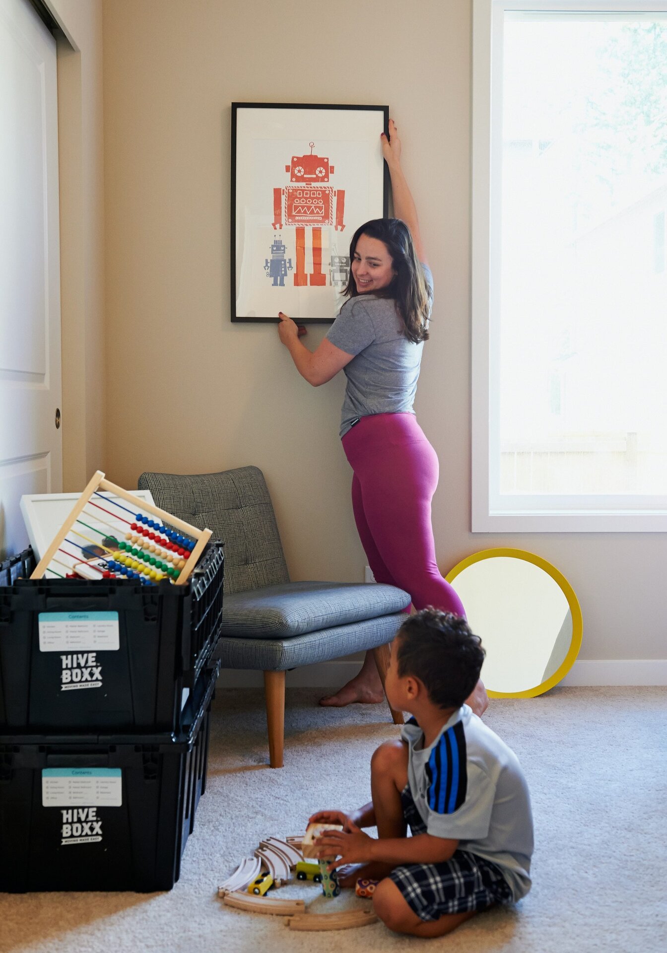 mother hanging a picture in a house with child watching