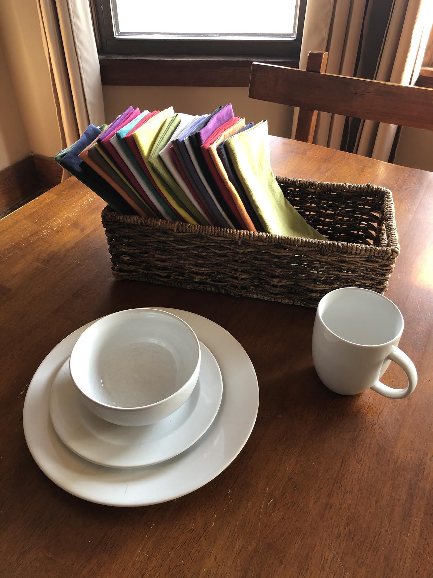 multicolored cloth napkins, white mug, white bowl, and white plate on a wooden kitchen table