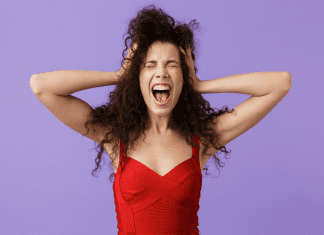 woman standing with hands on head and looking overwhelmed on lilac background