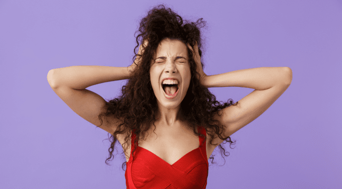 woman standing with hands on head and looking overwhelmed on lilac background