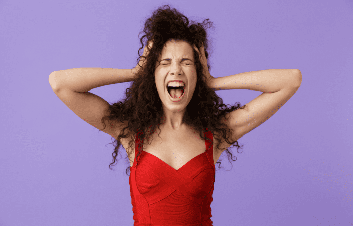 woman standing with hands on head and looking overwhelmed on lilac background