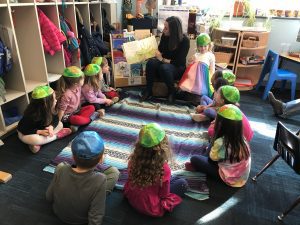 Children sitting in a circle listening to a parent reading a book