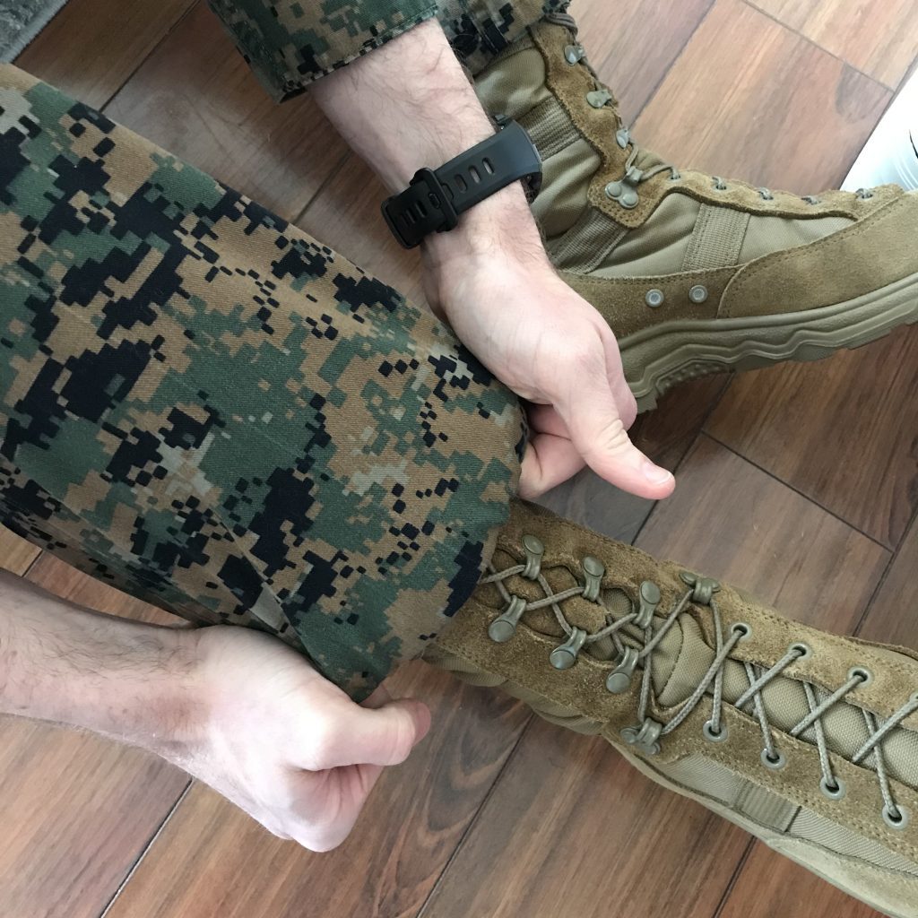 two hands pulling down uniform pants over brown boots 