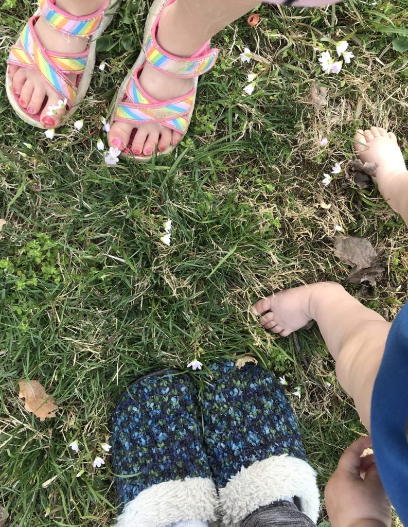 three pairs of feet: one small girls painted pink toes in rainbow sandals, baby toes in the middle, and a blue pair of slippers