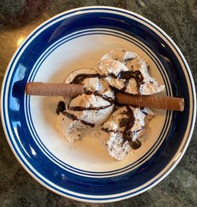 A bowl containing cookies and cream ice cream, chocolate sauce and two wafers.