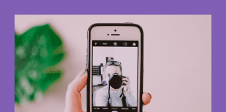 woman taking a selfie with camera and phone on a pink background and green plant shadowed behind it