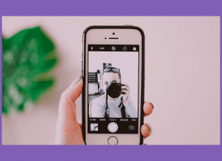 woman taking a selfie with camera and phone on a pink background and green plant shadowed behind it