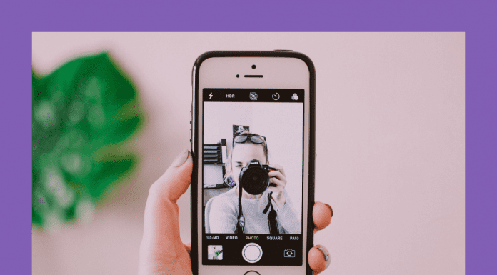 woman taking a selfie with camera and phone on a pink background and green plant shadowed behind it