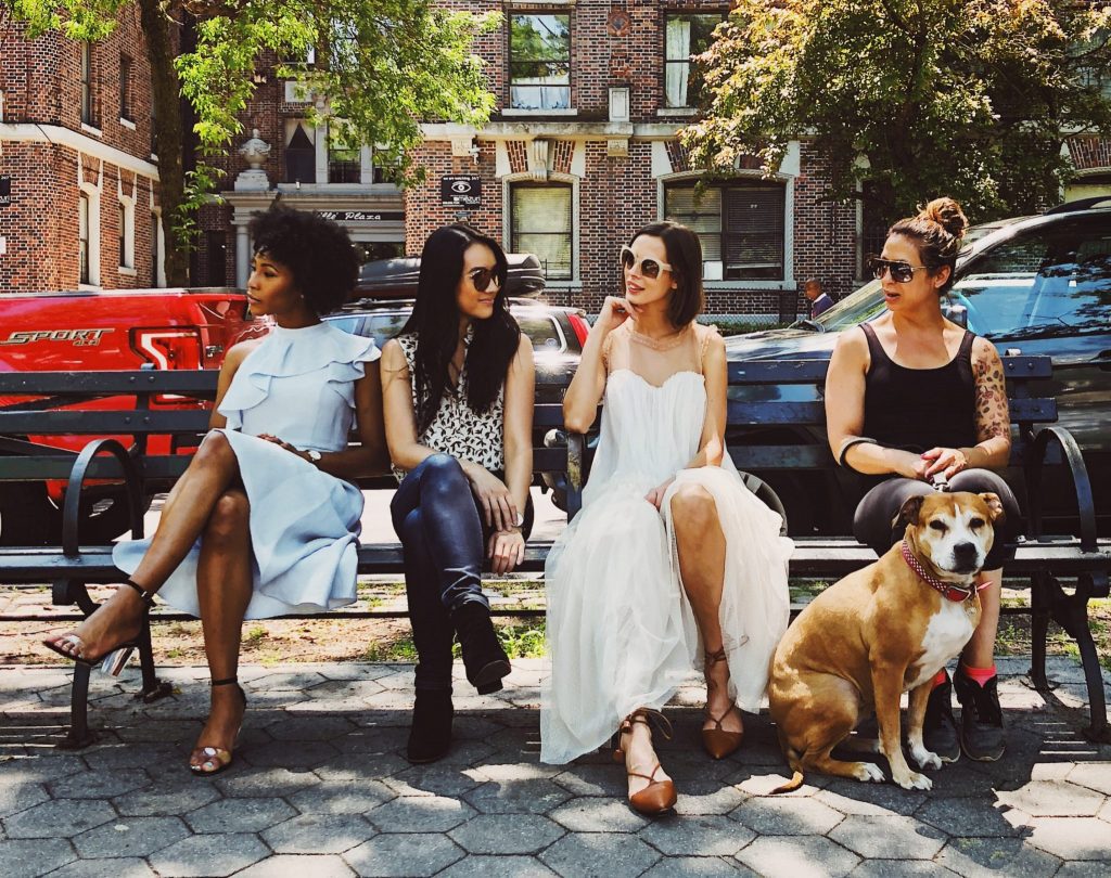 a group of women sitting on a bench with a dog in a city