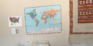 Homeschooling After Covid (and Perhaps Permanently) child in blue dress sitting on couch reading a book with maps behind her on the wall