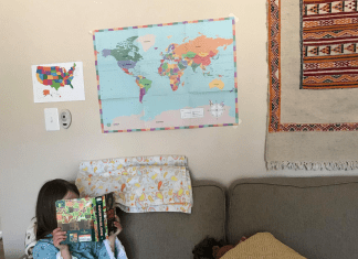 child in blue dress sitting on couch reading a book with maps behind her on the wall