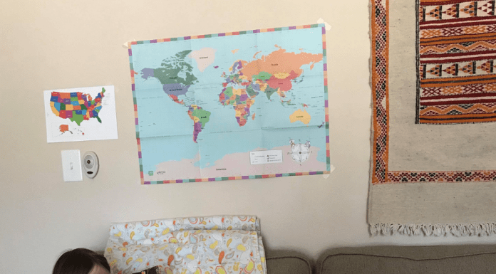 child in blue dress sitting on couch reading a book with maps behind her on the wall