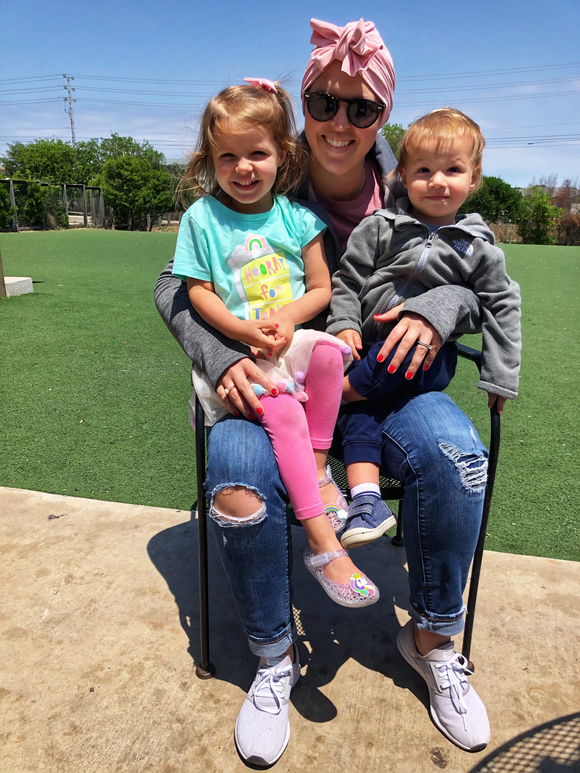 mother with a scarf on head holding two children on a sunny day