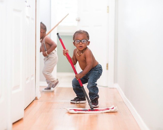 Two young boys mopping a wood floor in a house