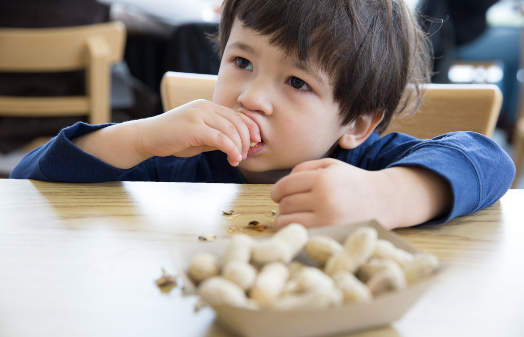 small boy eating peanuts at a table