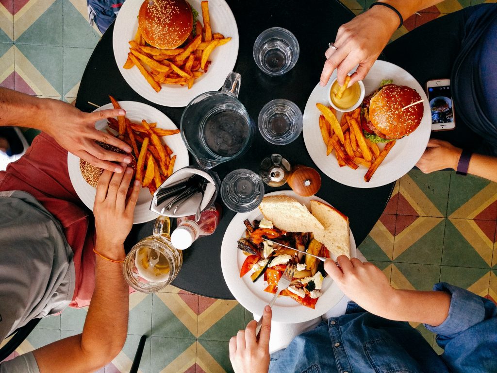 four people eating at table with various foods