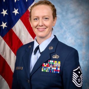 Female Veteran, Sarah Loicano, in AF uniform smiling in front of a flag.