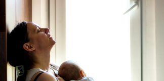 Woman holding infant appearing tired, concerned, sad, depressed