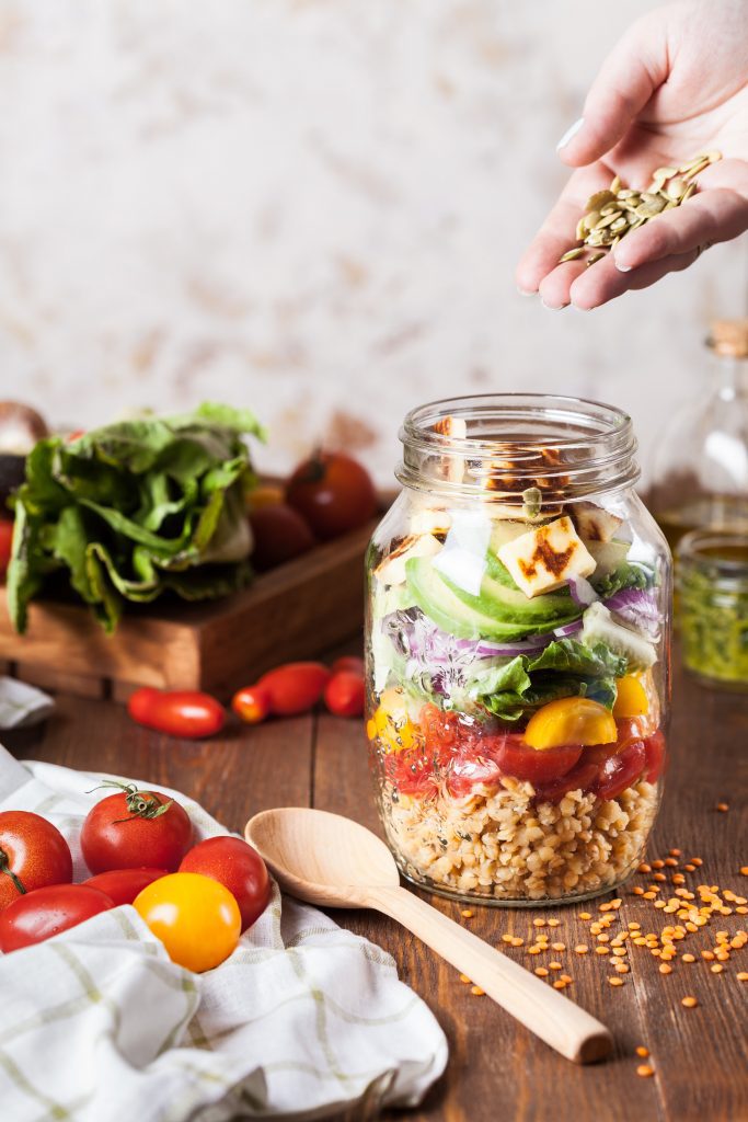 various vegetables on a cutting board with a spoon and jar for a salad in a jar meal