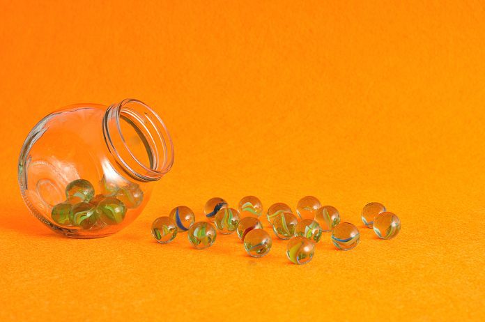 A,Collection,Of,Marbles,In,A,Glass,Jar,Displayed,On A jar of marbles tipped on its side with many marbles spilled out