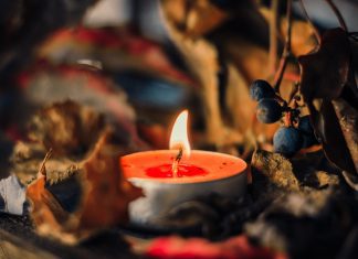 A lit orange tea light candle surrounded by fall leavess and